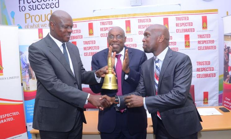 Uganda Breweries Out going Managing Director Mark Ocitti (L) hands over The Bell to the new UBL Managing Director Alvin Mbugua (R). Looking on is Japeth Katto the UBL Board Chairman.